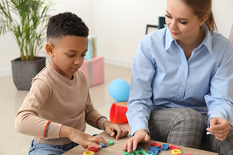 This is a stock photo from Shutterstock. An adult woman sits next to a young boy who is playing with alphabet letters. 