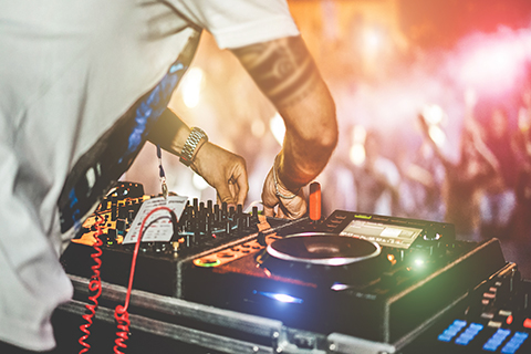 This is a stock photo from Shutterstock. The is a up close image of a set of turn tables and sound equipment in a DJ booth. The DJ booth is overlooking a crowd.
