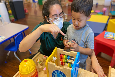 This photo was provided by the University of Miami & Nova Southeastern University Center for Autism and Related Disabilities. A student is speaking with a young patient playing with toys.