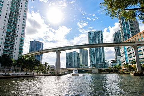 This is a stock photo from Shutterstock. The view is from the Miami River facing a bridge and various high-rise buildings. There is also a boat in the water.