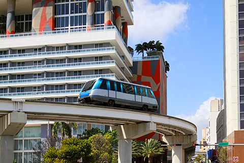 This is a stock photo from Shutterstock. This image is focused on a Metro Mover car. The metrorail system in downtown Miami is above ground. Behind the metro mover car is a high-rise condominium building.